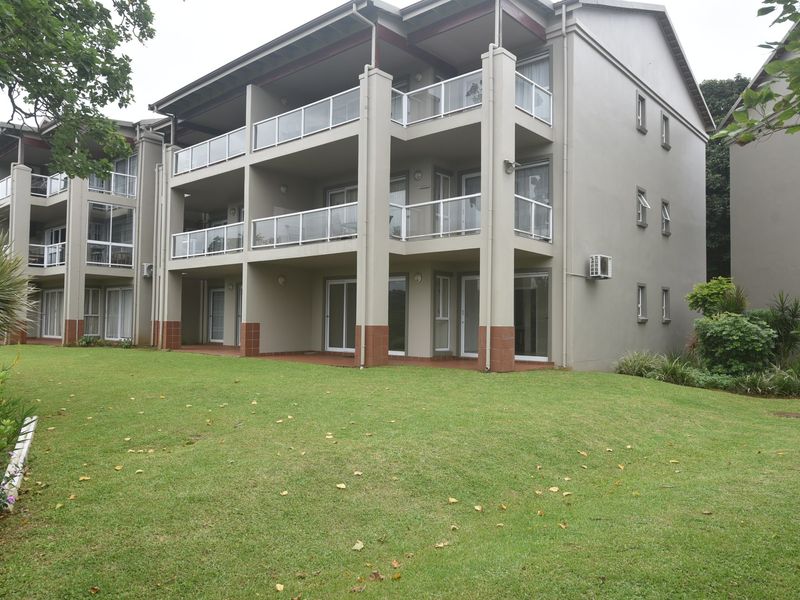 Rear view of a multi-story apartment complex featuring private balconies with glass balustrades, sliding glass doors, and well-maintained communal lawn areas.