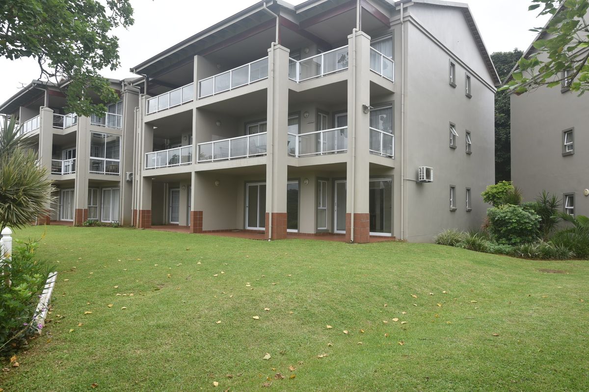 Rear view of a multi-story apartment complex featuring private balconies with glass balustrades, sliding glass doors, and well-maintained communal lawn areas.