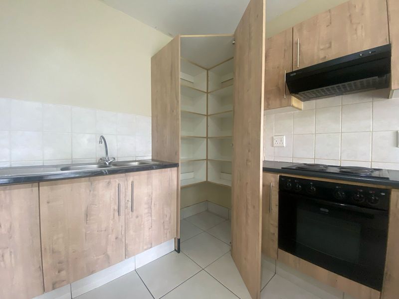 A functional kitchen featuring light wood-finish cabinetry, a built-in oven with extractor fan, tiled backsplash, and a convenient corner pantry cupboard.