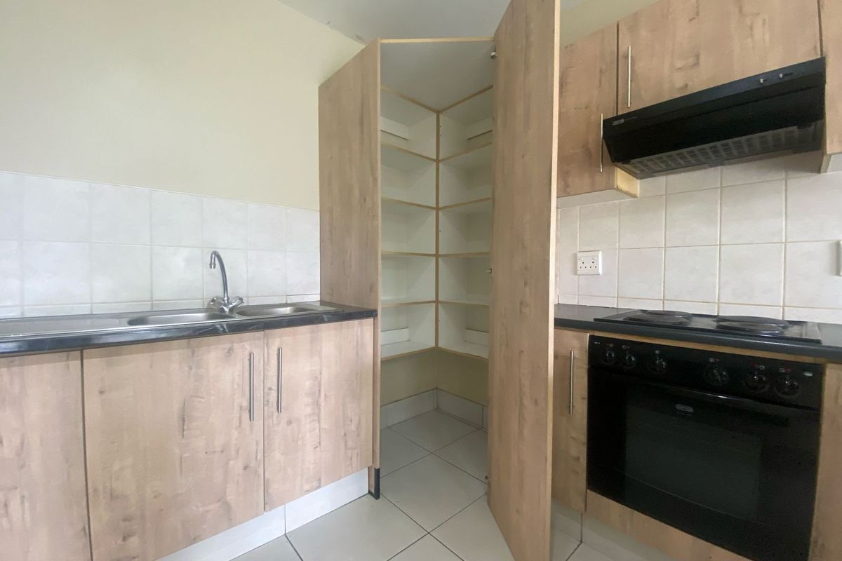 A functional kitchen featuring light wood-finish cabinetry, a built-in oven with extractor fan, tiled backsplash, and a convenient corner pantry cupboard.