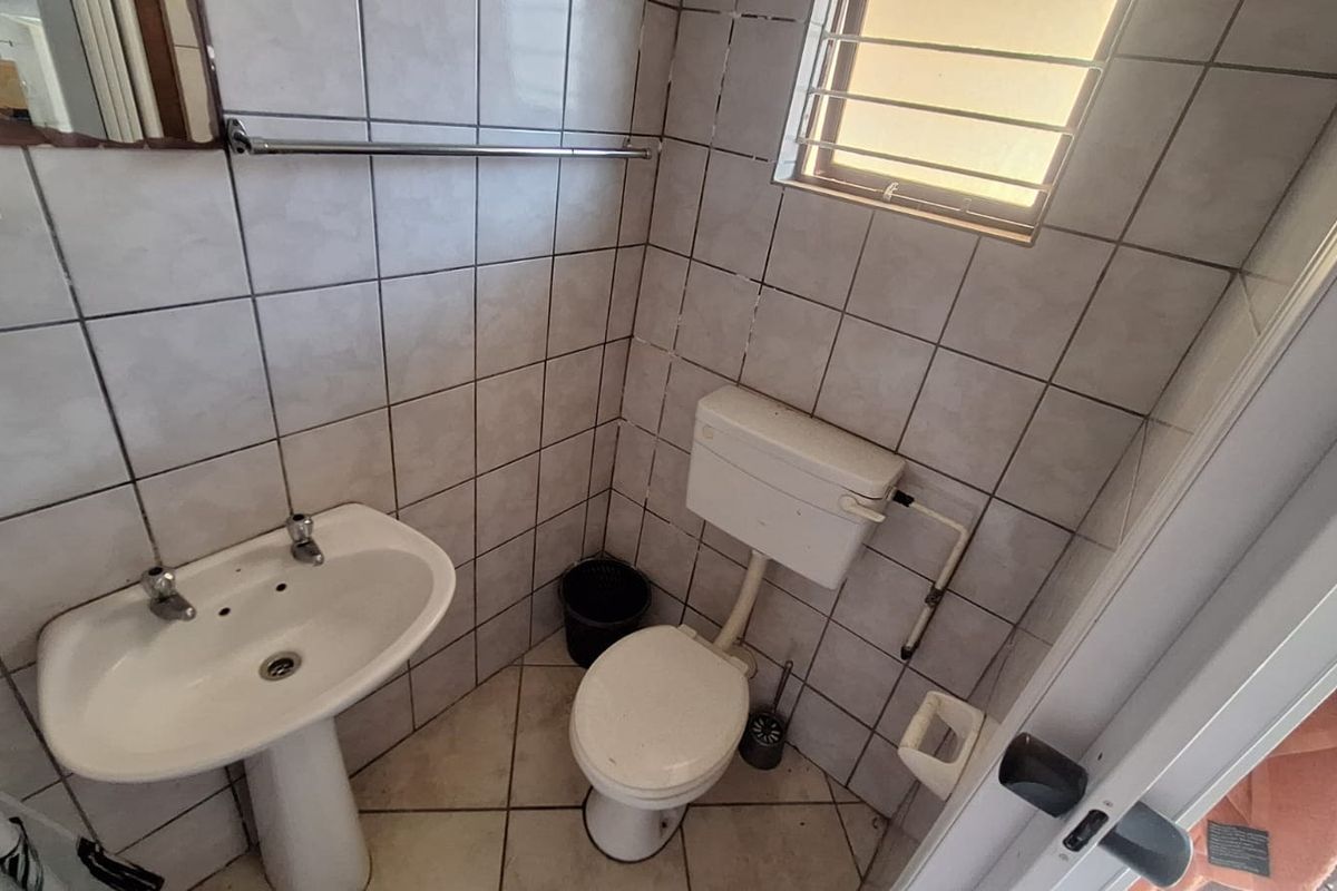 A compact bathroom featuring a pedestal basin, standard toilet, and full-height wall tiling.
