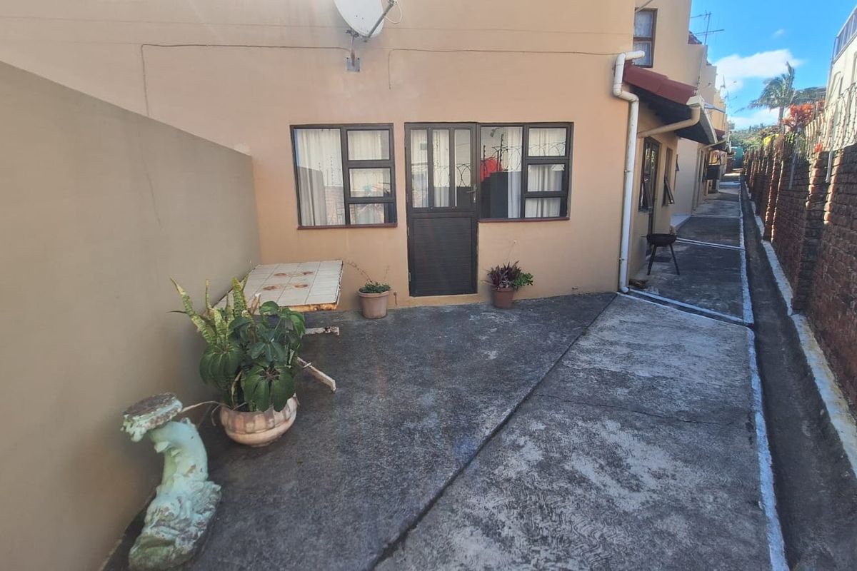 A rear exterior view of the apartment featuring a concrete paved courtyard area, brick boundary wall, and access to the rear entrance.