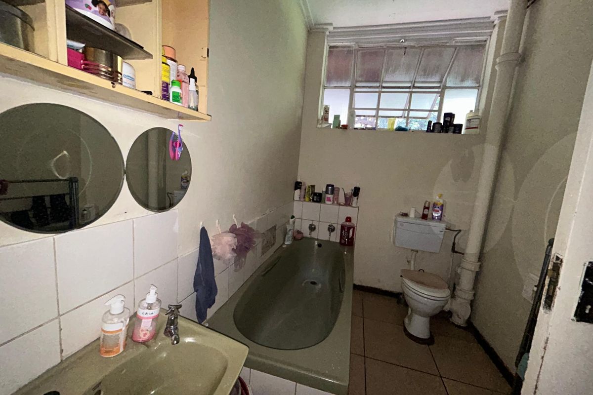 A dated bathroom featuring a built-in bathtub, pedestal basin, and toilet, with tiled flooring and splashbacks, requiring cosmetic updates to modernize the space.