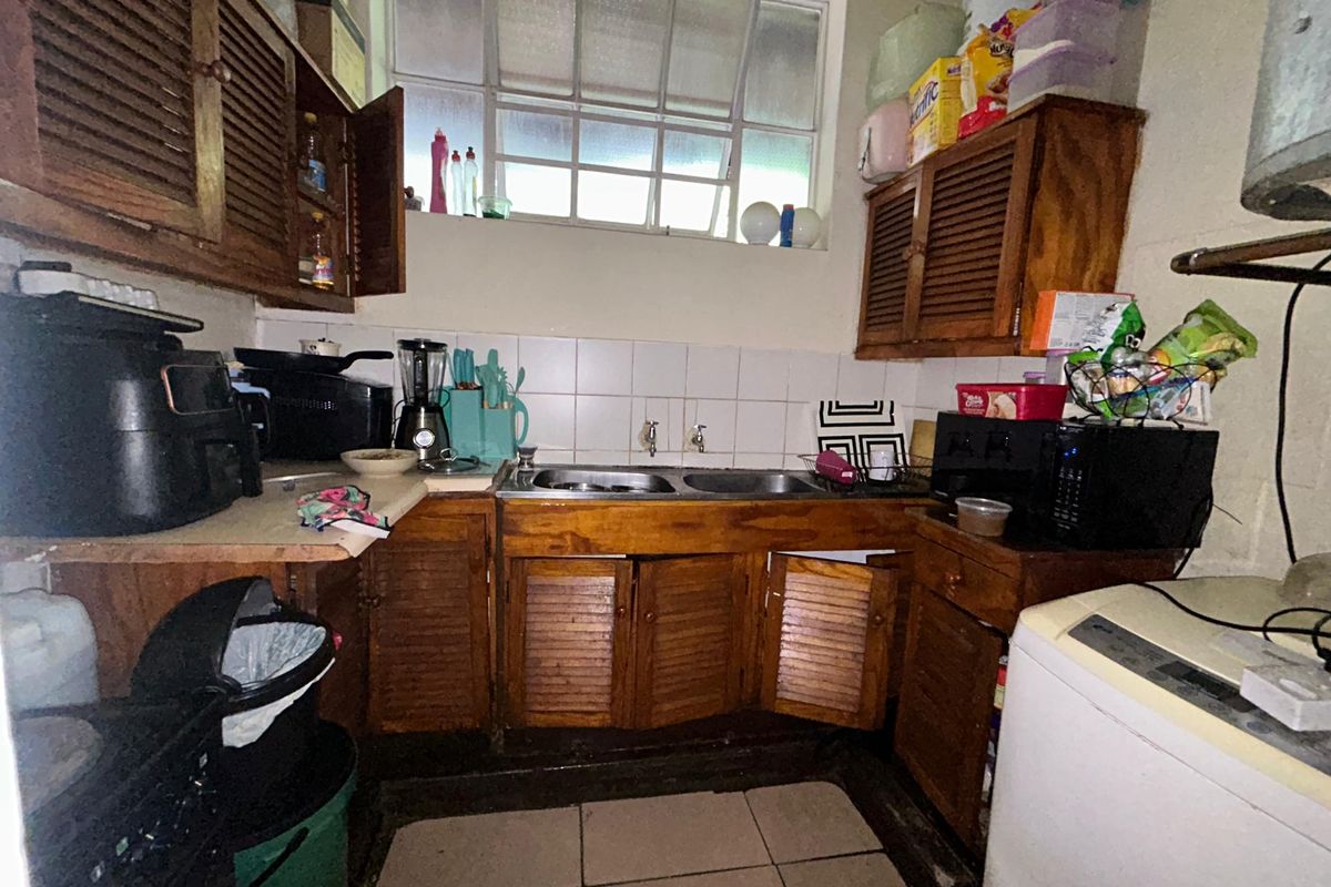 A compact kitchen featuring wooden cabinetry, a double basin sink, and tiled splashbacks, currently requiring significant maintenance and cosmetic updates.