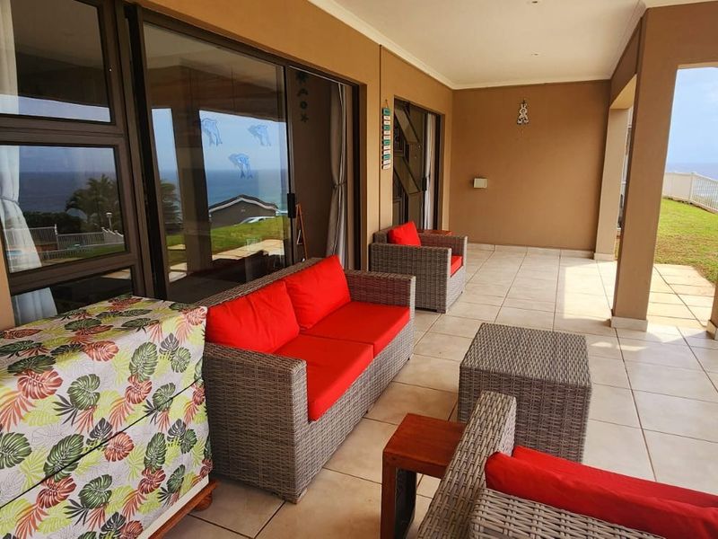 A spacious covered patio featuring tiled flooring and sliding glass doors, offering an outdoor living area with scenic coastal views.