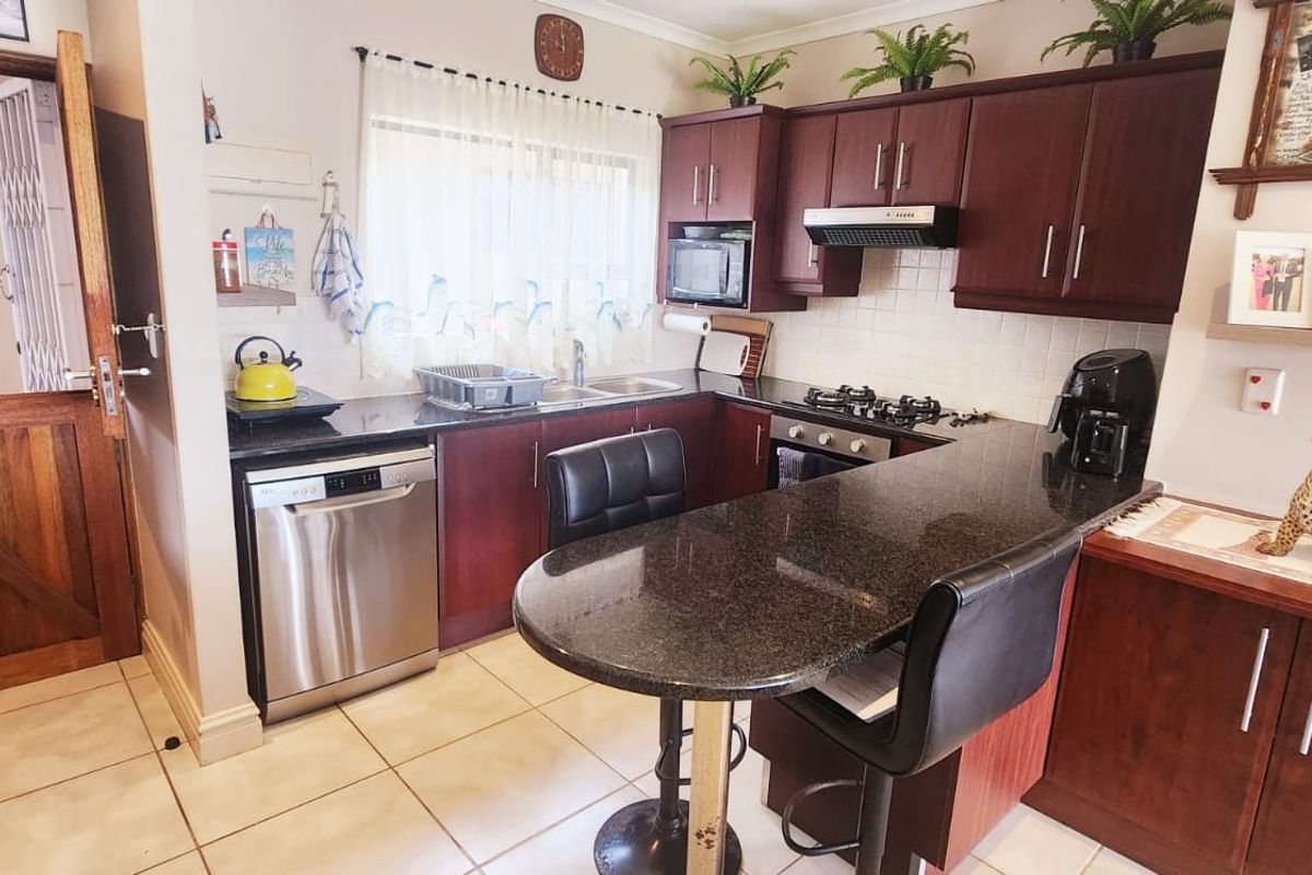 Functional kitchen featuring dark wood cabinetry, granite countertops, a breakfast bar, gas hob, and integrated oven, with durable tiled flooring throughout.