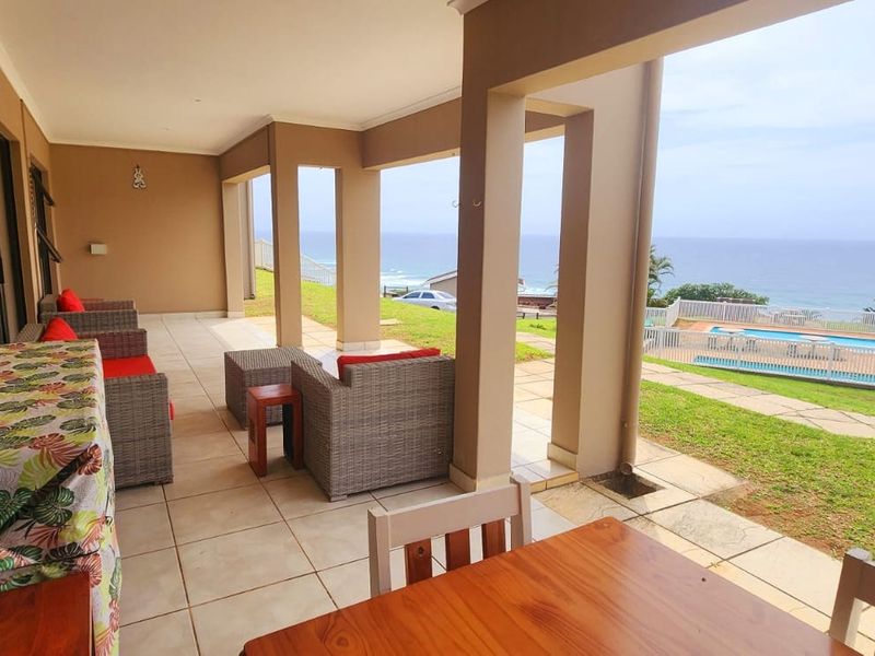 Spacious covered patio featuring tiled flooring and structural pillars, offering direct access to the garden and scenic ocean views.