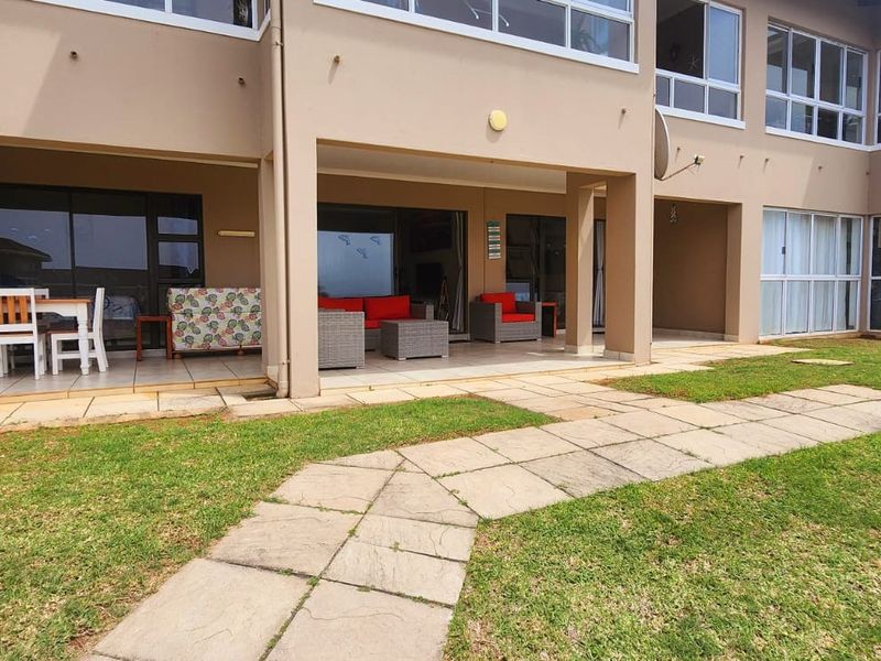 A spacious ground-floor apartment featuring a covered tiled patio with direct access to a shared lawn and paved garden walkway.