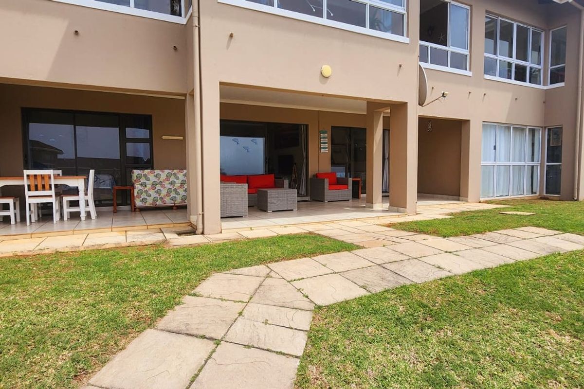 A spacious ground-floor apartment featuring a covered tiled patio with direct access to a shared lawn and paved garden walkway.