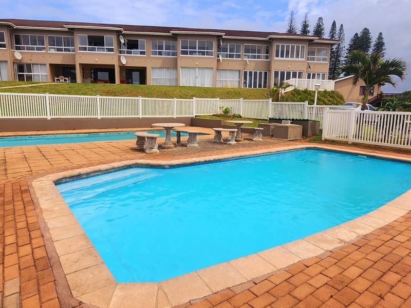 Communal swimming pool area with paved decking and white perimeter fencing, set against the backdrop of an apartment complex.