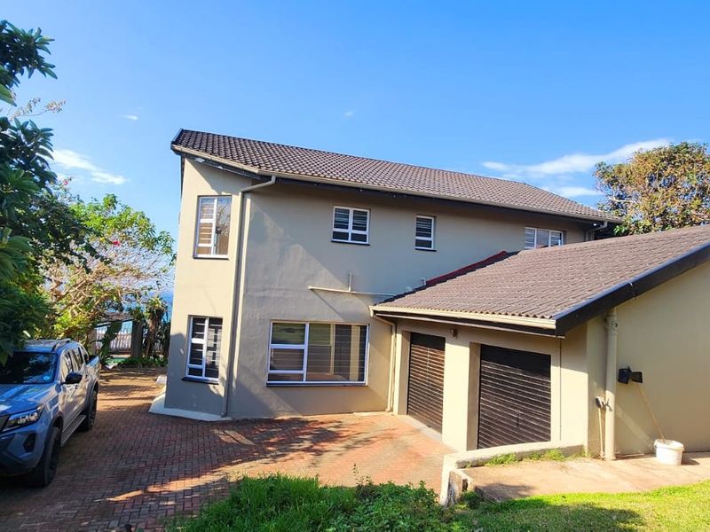 A two-story residential property featuring a paved driveway, double garage, and tiled roof, set within a landscaped garden area.