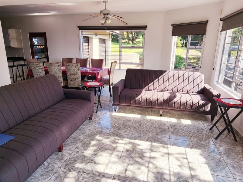 Spacious open-plan living and dining area featuring tiled flooring, ceiling fan, and large windows with security bars and roller blinds.
