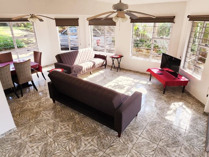 Bright open-plan living and dining area featuring tiled flooring, multiple large windows with blinds, and dual ceiling fans.