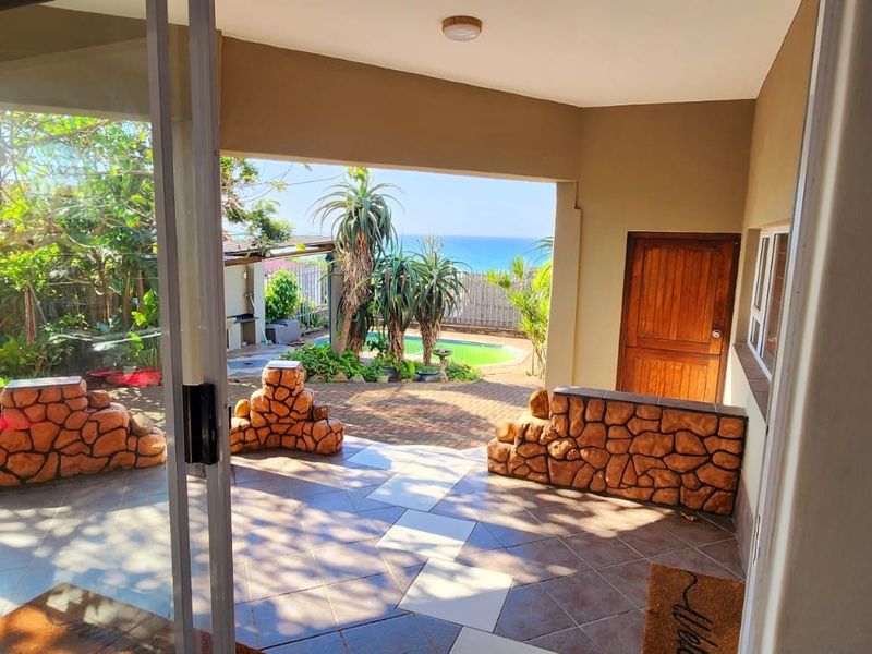 Covered patio area featuring tiled flooring, stone-clad feature walls, and direct access to the garden and pool area with ocean views.