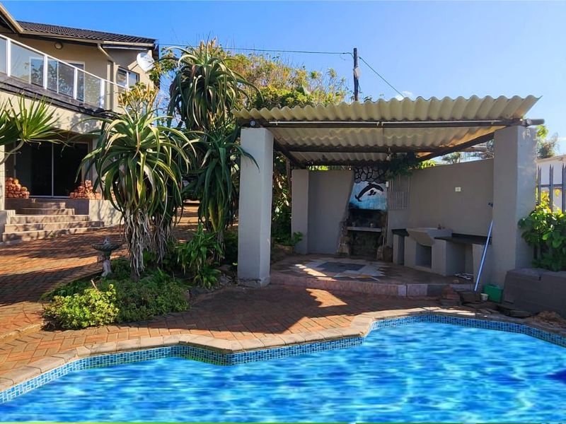 Outdoor entertainment area featuring a swimming pool, paved deck, and a covered patio with a built-in braai facility.