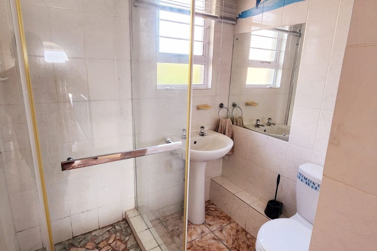 A compact bathroom featuring a pedestal basin, toilet, and a glass-enclosed shower with tiled finishes throughout.