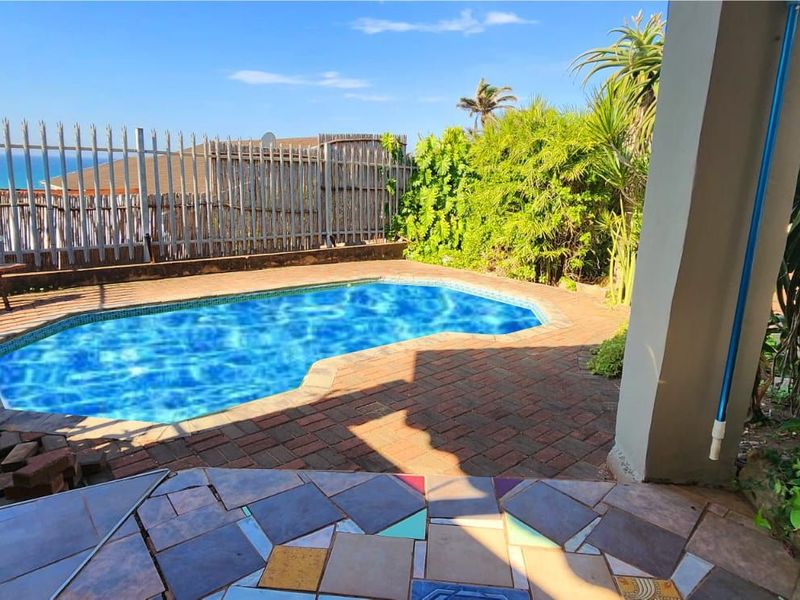 Outdoor pool area featuring a swimming pool, brick paved surround, and tiled patio space with security fencing.