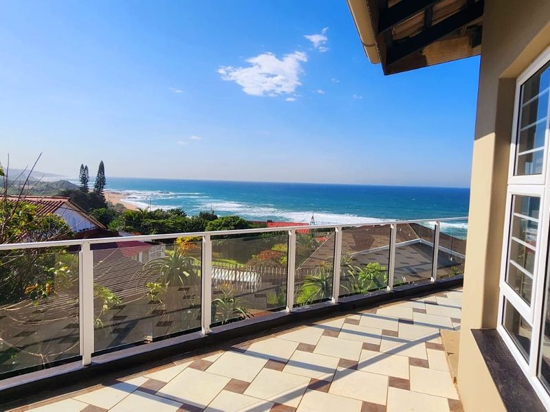 Spacious balcony featuring a modern glass balustrade and tiled flooring, offering expansive, unobstructed views of the coastline and ocean.