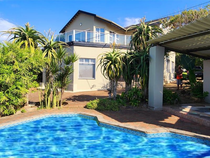 Outdoor pool area featuring a paved deck, covered patio space, and a balcony with glass balustrades overlooking the garden.