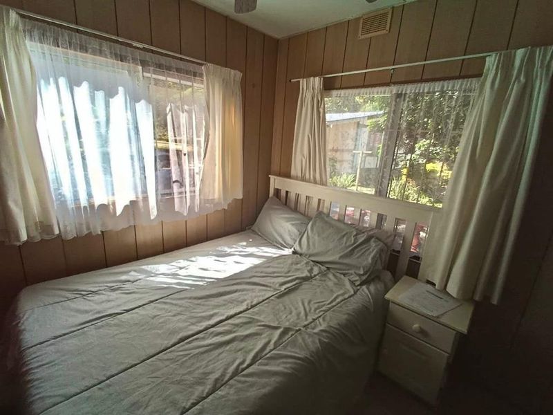 A bedroom featuring dated wood paneling, a ceiling fan, and dual windows allowing natural light.