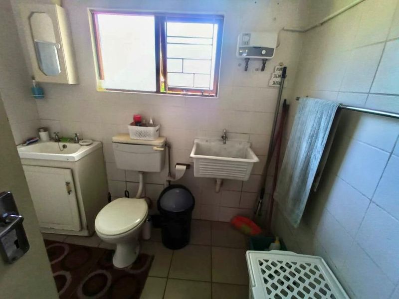 A functional laundry room featuring a ceramic utility sink, vanity basin, toilet, and tiled finishes, offering potential for modernization and improved utility space design.