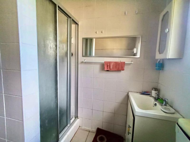 A functional bathroom featuring a shower enclosure, vanity basin, and wall-mounted medicine cabinet with tiled finishes throughout.