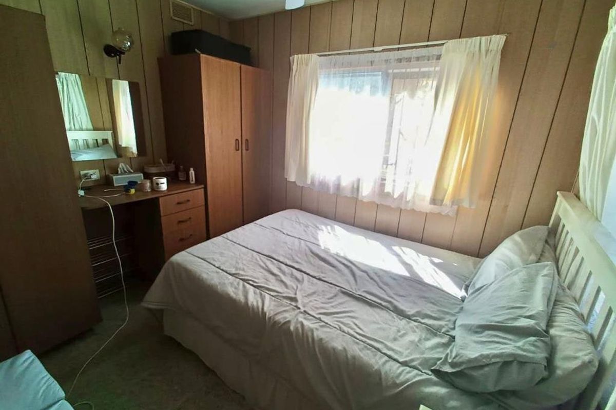 A bedroom featuring dated timber wall paneling and a ceiling fan, offering a blank canvas for modern renovation and interior updates.