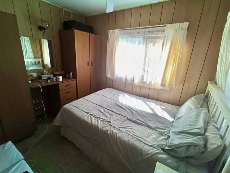 A bedroom featuring dated timber wall paneling and a ceiling fan, offering a blank canvas for modern renovation and interior updates.