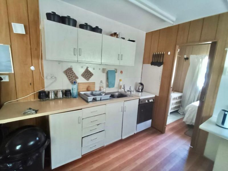 A functional kitchen featuring built-in cabinetry, laminate countertops, and a built-in oven, with wood-paneled walls and direct access to an adjacent room.