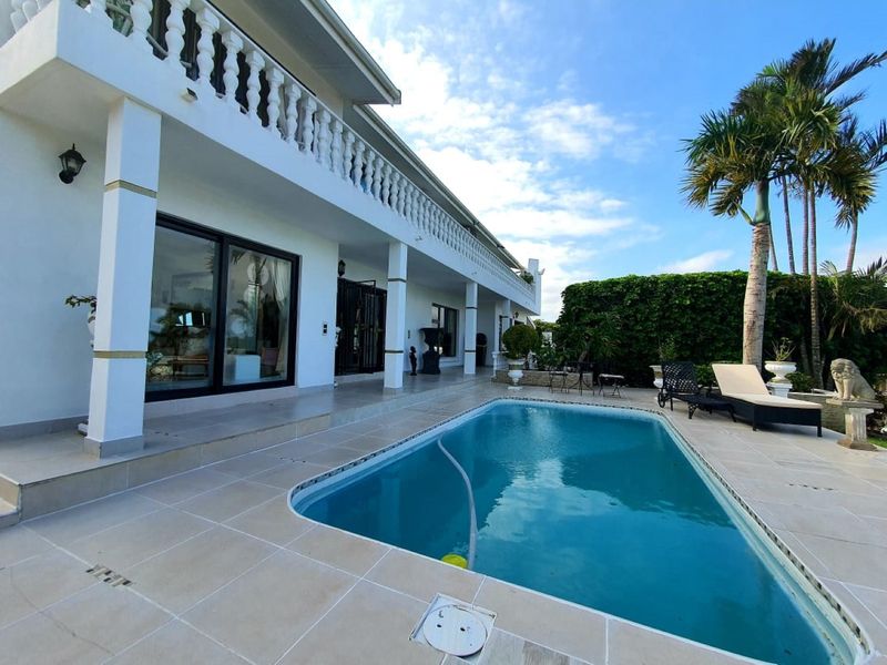 Spacious outdoor pool area featuring a tiled patio, covered veranda with balustrade, and direct access to the main living areas through sliding glass doors.