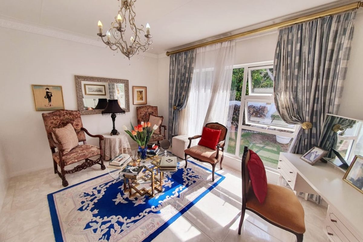 A bright and inviting living room featuring tiled flooring, decorative crown molding, and large windows that provide ample natural light and garden views.