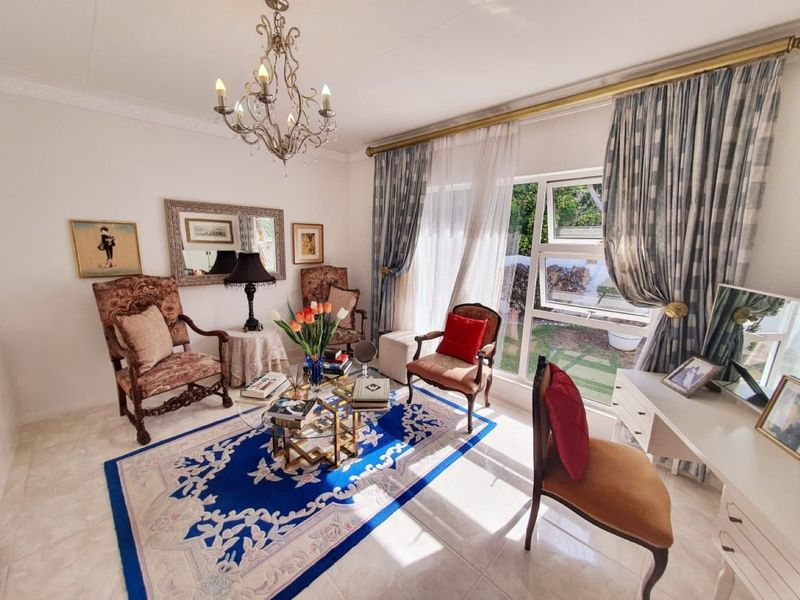 A bright and inviting living room featuring tiled flooring, decorative crown molding, and large windows that provide ample natural light and garden views.