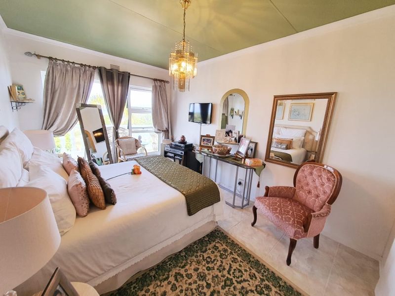 A well-lit bedroom featuring tiled flooring, a decorative chandelier, and large windows providing natural light and access to an outdoor area.