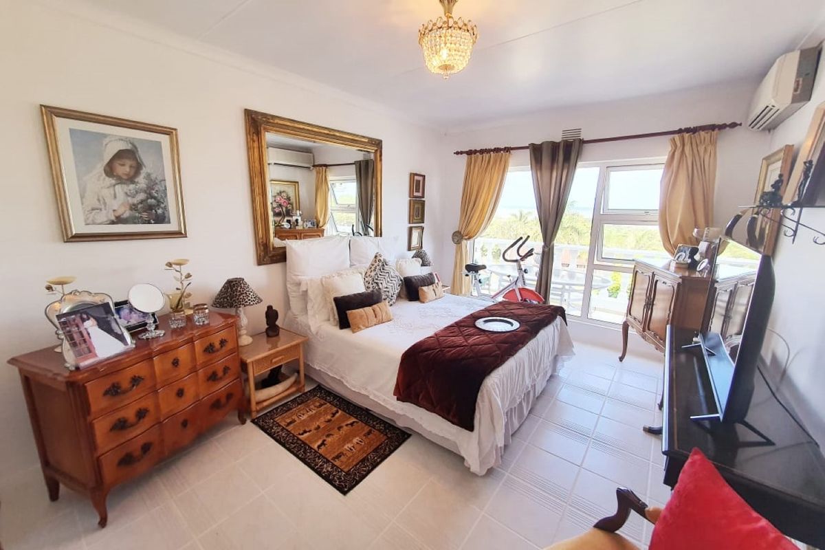 A well-lit bedroom featuring tiled flooring, a wall-mounted air conditioning unit, and large windows providing natural light and access to an outdoor area.