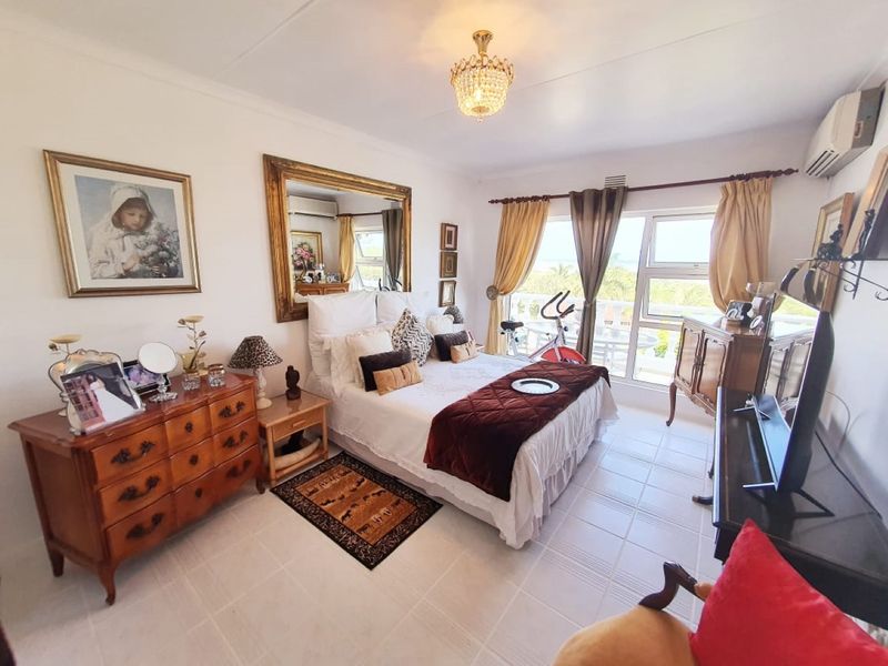 A well-lit bedroom featuring tiled flooring, a wall-mounted air conditioning unit, and large windows providing natural light and access to an outdoor area.