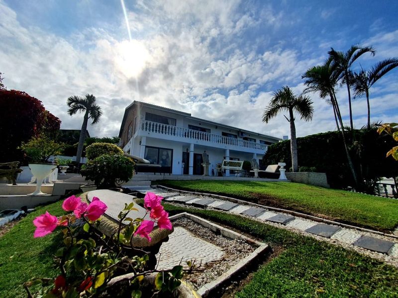 Rear view of a two-story house featuring a spacious balcony, landscaped garden with stone pathways, and mature palm trees.