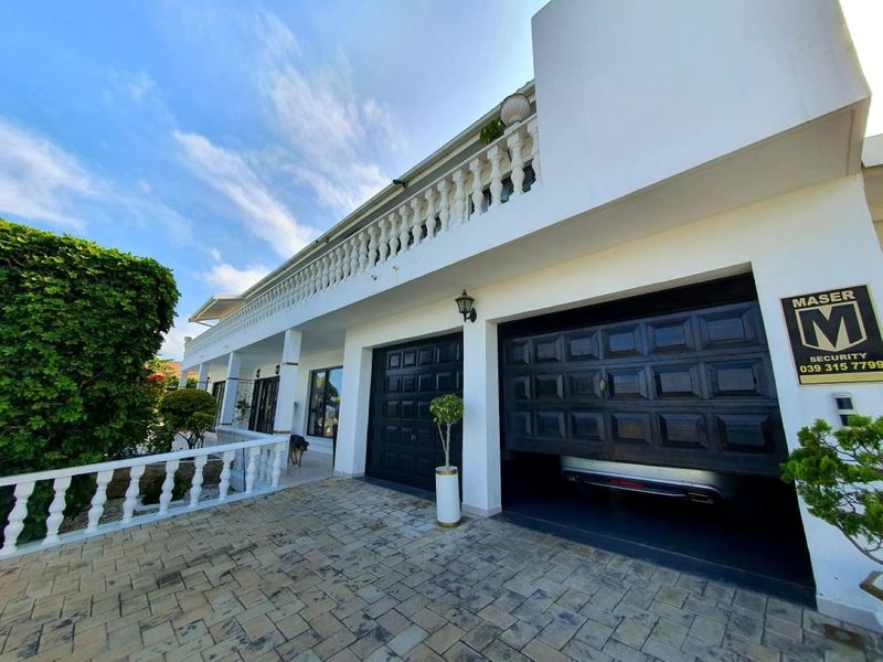 Front exterior view of the property featuring a paved driveway, double garage with black doors, and a balcony with decorative balustrades.