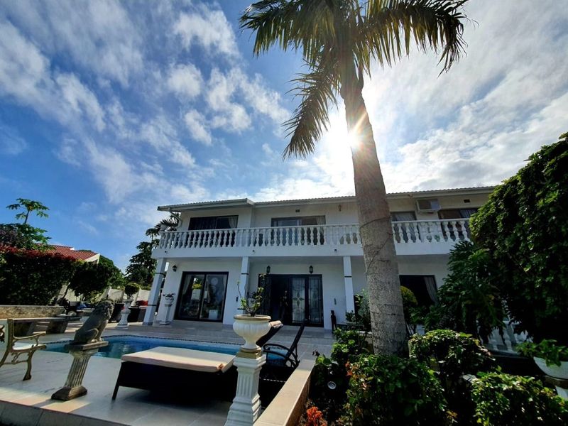 Rear view of a two-story house featuring a swimming pool, a spacious balcony with balustrades, and established garden landscaping.