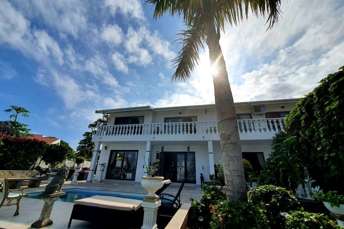 Rear view of a two-story house featuring a swimming pool, a spacious balcony with balustrades, and established garden landscaping.