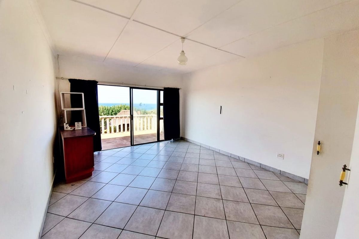 A bright, open-plan living area featuring tiled flooring and large sliding glass doors that open onto a balcony with ocean views.