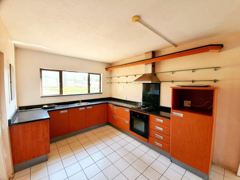 A functional kitchen featuring wooden cabinetry, black countertops, a built-in oven, hob, and extractor fan with tiled flooring and glass shelving.