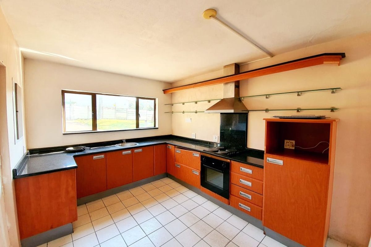 A functional kitchen featuring wooden cabinetry, black countertops, a built-in oven, hob, and extractor fan with tiled flooring and glass shelving.