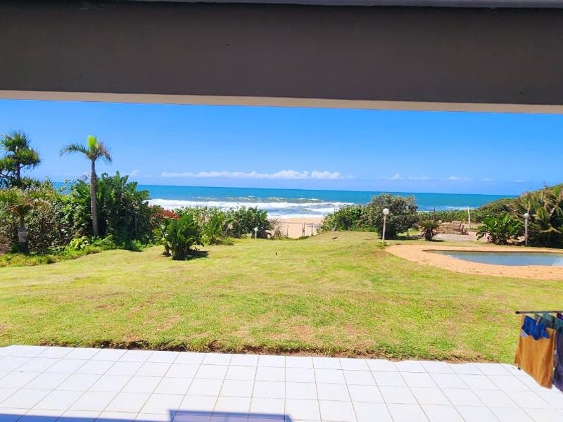 A covered patio overlooking a spacious garden with a swimming pool and direct ocean views.