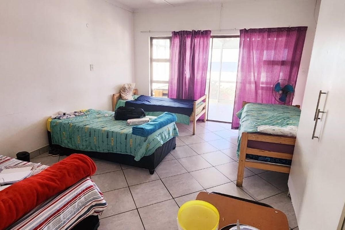 A spacious bedroom featuring tiled flooring, built-in cupboards, and large sliding glass doors providing access to an outdoor area.