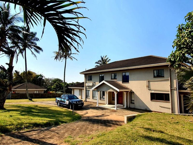 A well-maintained two-story residential property featuring a paved driveway, covered entrance porch, and a spacious front garden with mature palm trees.