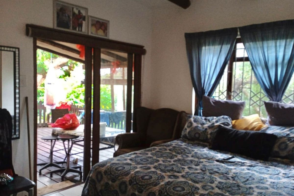 A bedroom featuring exposed ceiling beams, tiled flooring, and a sliding glass door providing direct access to an outdoor patio area.