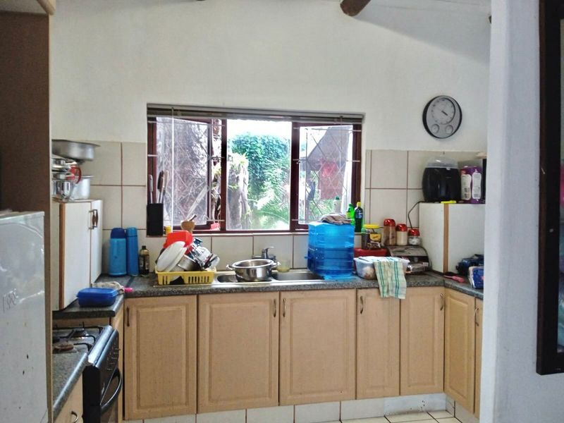 A functional kitchen featuring light wood cabinetry, granite countertops, a double sink, and a gas stove, with a window overlooking the garden.