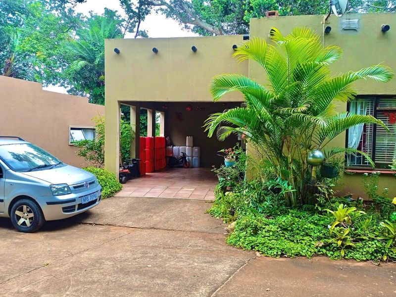 Front elevation of the townhouse featuring a covered carport, concrete driveway, and established garden area.