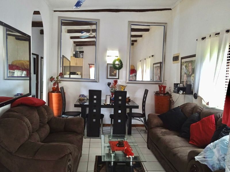 Open-plan living and dining area featuring exposed timber ceiling beams, ceramic floor tiles, and a traditional archway connecting to adjacent spaces.