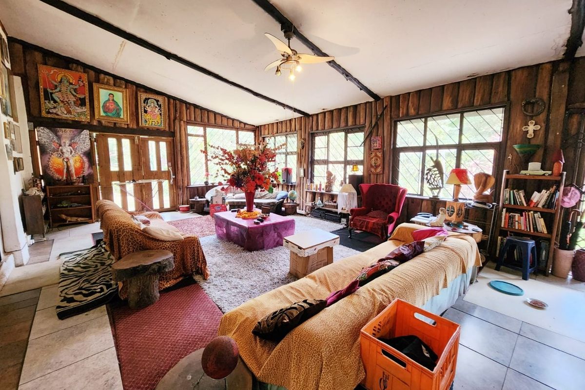 Spacious living room featuring rustic exposed timber walls, exposed ceiling beams, large windows providing natural light, and tiled flooring.